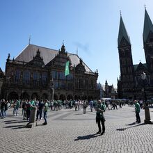 Foto des Bremer Rathaus bei Sonnenschein. Auf dem Platz davor ist reges Treiben. Viele Menschen sind zu sehen, Restaurants haben ihre Außengastonomie geöffnet.