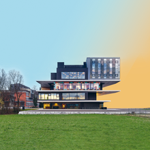 Foto eines modernen dreistöckigen Gebäudes. Davor eine große Rasenfläche. Das Foto wurde in Teilen verändert. So ist rechts hinter dem Haus statt des ursprünglichen Hintergrundes eine gelbe Fläche zu sehen, die in den blauen Himmel übergeht.