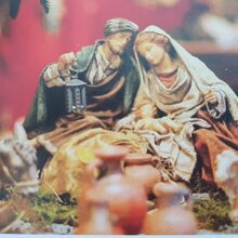 Nahaufnahme von Krippenfiguren. Zusehen sind Maria und Joseph mit dem Jesuskind. Im Vordergrund sind verschwommen drei Schafe auf der linken Seite, in der Mitte vier Tonkrüge und auf der rechten Seite ein Esel zu sehen. Die Figuren sind sehr filigran.