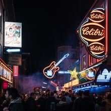 Foto von der Reeperbahn. Es ist dunkel. Auf der Straße stehen Trauben mit Menschen. Rechts und links an den Häuserfassaden strahlen bunt Leuchtreklamen.