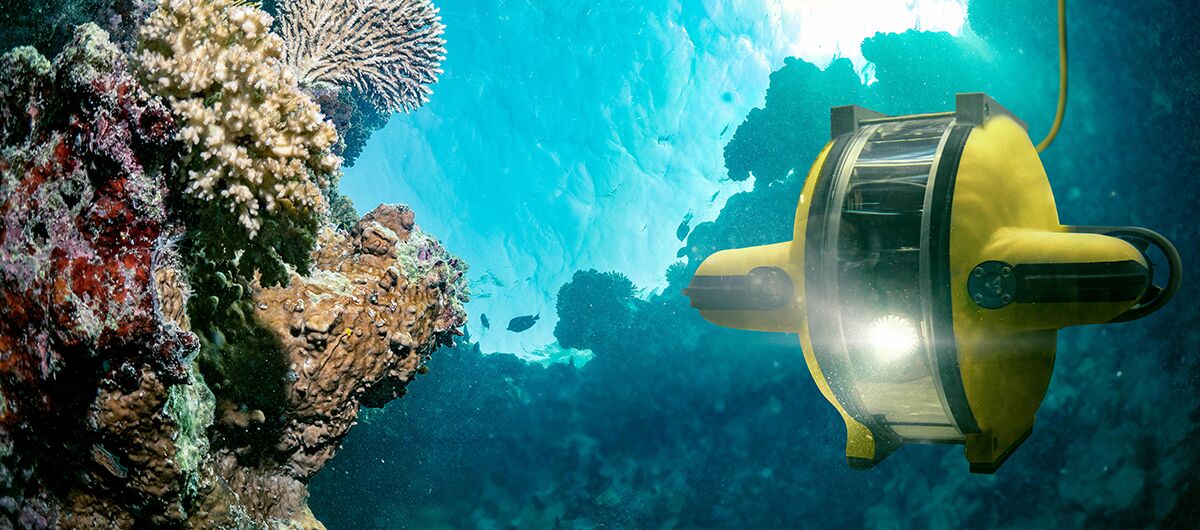 Foto eines Unterwasserroboters, der die Tiefsee erforscht. Auf der linken Fotoseite sind Felsen, auf denen Korallen leben, zu sehen. Die rechte Fotoseite wird durch den Roboter dominiert.