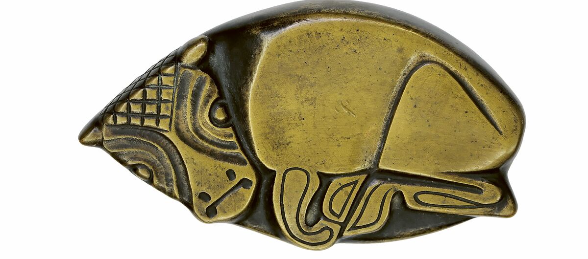 Foto einer Tierplastik. Zu sehen ist ein liegendes Kälbchen. Die metallische platte Plastik ist auf den erhobenen Flächen golden, die tieferliegenden Flächen sind schwarz.