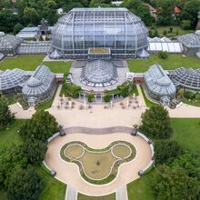Luftaufnahme der Gebäude des Botanischen Gartens Berlin. Zentral steht ein kuppelartiges großes Glashaus. Davor rechteckig angeordnet stehen neun kleinere Glashäuser in unterschiedlichen Formen, die durch kurze Gänge miteinander verbunden sind.