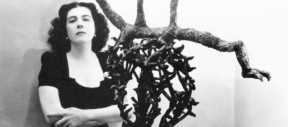 Schwarz-weiß Foto von Maria Martins, die mit verschränkten Armen hinter ihrer Skulptur Ma Chanson steht.