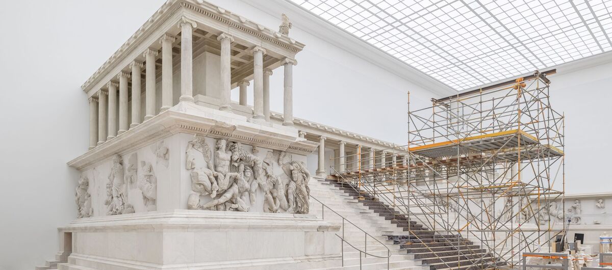 Das Foto zeigt den Pergamonaltar von der linken Seite aus. Mittig auf der hochsteigenden Treppe ist ein Baugerüst aufgebaut. Rechts im Bild lagern Elemente des Altars teil eingepackt.