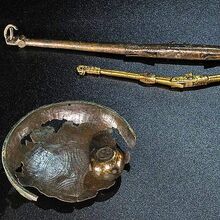 Foto metallischer Teile von Klappwaagen mit Schalen und Gewichten auf schwarzem Untergrund. Oben liegen eine große und eine kleine Klappwaage , links eine löchrige Schale mit einem Gewicht, daneben zwei weitere kugelförmige Gewichte.