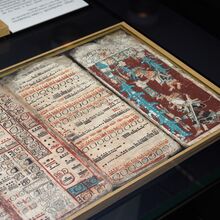 Fot einer Maya-Handschrift. Auf einem schwarzen Untergrund liegt in einem hellen dünnen Holzrahmen mit verschiedenen Faarben beschrieben und bemalte Papiere. Die Ecken der Seiten sind abgenutzt.