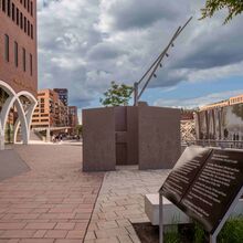 Foto mit dem Blick auf das denk.mal Fruchtschuppen C vor dem Westfield Hamburg-Überseequartier. Es besteht aus braunen zirka zwei Meter hohen Metallwänden, die unsystematisch zueinander stehen. Im Vordergrund des Fotos steht eine Informationstafel.
