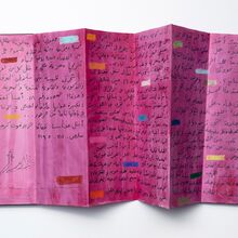 Foto eines rot angemalten Papiers im Querformat, das fünfmal senkrecht geknickt ist. Links unten in der Ecke ist ein Ansatz eines Baumes gezeichnet. Der Rest ist mit schwarzen Schriftzeichen beschrieben. Der Text wird durch bunte Rechtecke unterbrochen.