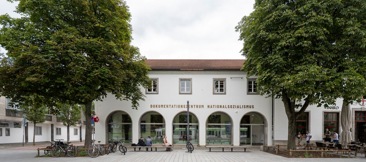 Foto der Außenansicht des Dokumentationszentrums Nationalsozialismus der Museen Freiburg. Fünf Rundbögen mit Fensterglas prägen die Hausfront im Erdgeschoss. Darüber ist der Schriftzug Dokumentationszentrum Nationalsozialismus zu lesen.