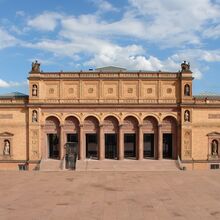 Foto des Eingangsportals der Hamburger Kunsthalle. Sechs Säulen dominieren die historische Steinfassade. Treppenstufen führen zu den Säulen. Zwischen der ersten und zweiten Säule von links sind die Treppen durch einen Fahrstuhl unterbrochen.