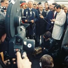 Willy Brandt steht draußen vor Mikrofonen. In der Hand hält er einen Zettel. Er spricht. Um ihn scharren sich Menschen, die teils Handmikrofone zu ihm und Videokameras auf ihn richten.